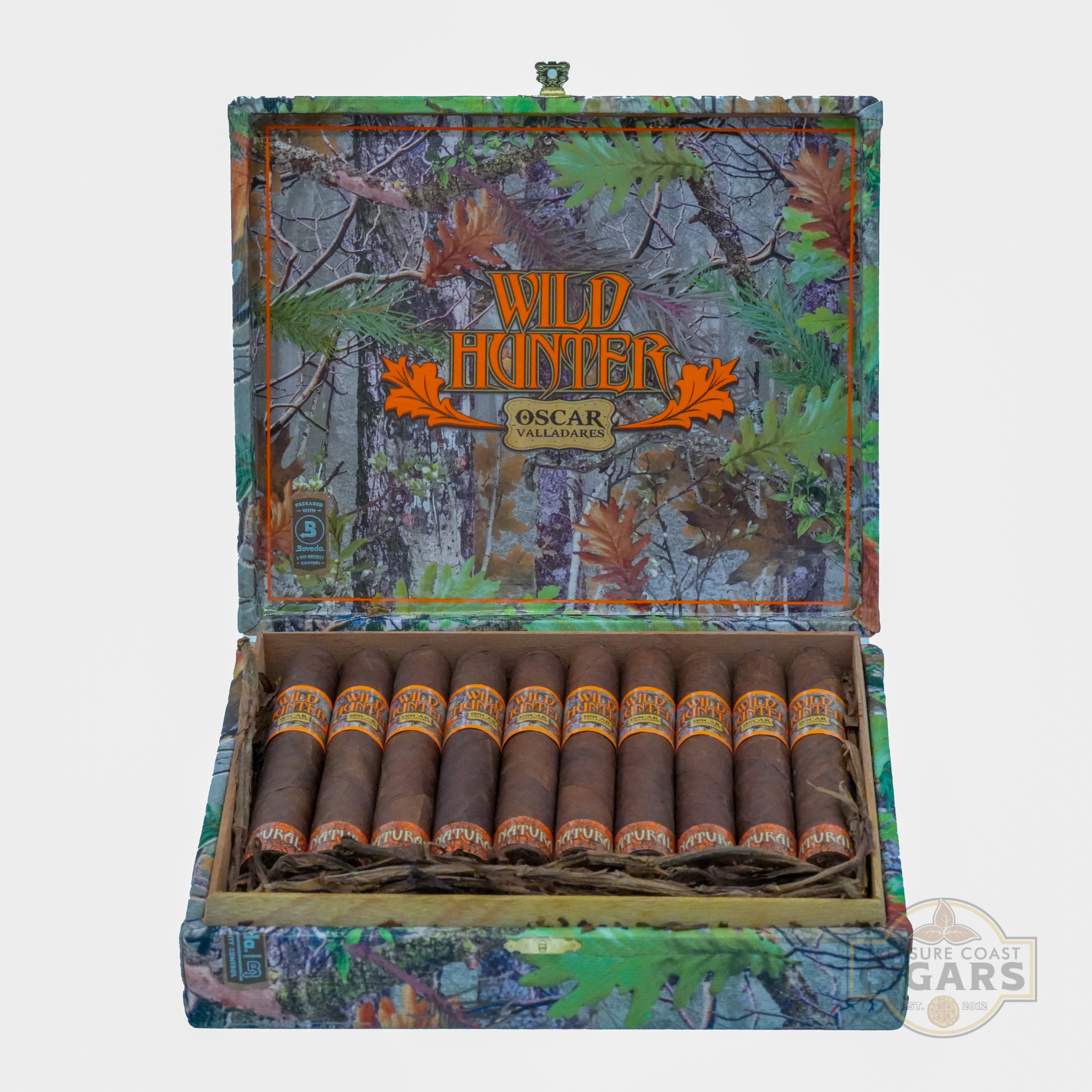 A box of "Wild Hunter Oscar Valladares" cigars is open, revealing ten dark brown cigars neatly arranged inside. The box features a camouflage pattern with green, brown, and orange hues, along with leaves and branches, and the brand name prominently displayed in bold orange letters. The interior of the box has a rustic design.